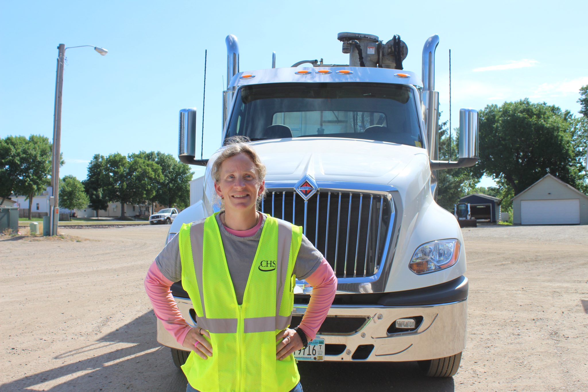 Woman wearing a yellow safety vest standing in front of a semi truck cab