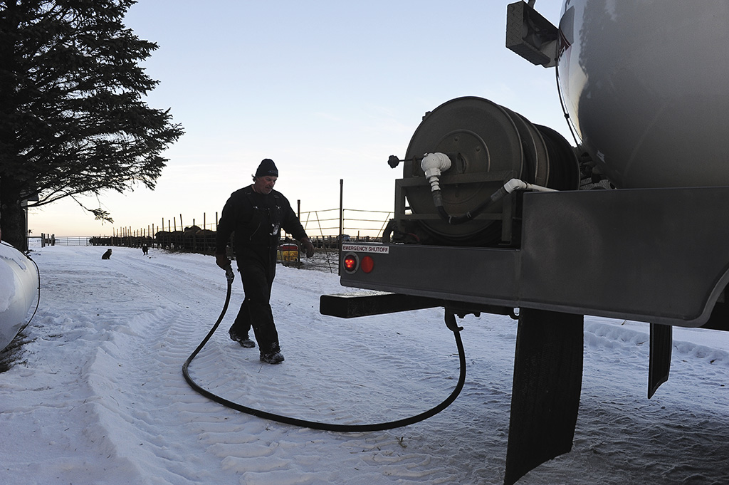 Man walking hose back to a propane truck on a snowy road